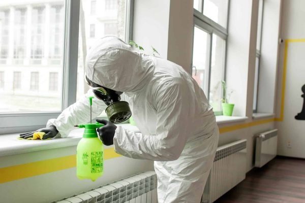 A man in protective equipment disinfects with a sprayer in the office. Surface treatment due to coronavirus covid-19 disease. A man in a white suit disinfects the room with a spray gun. Virus pandemic